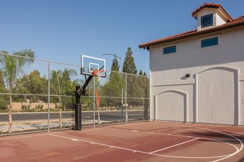 A basketball court with a hoop and a fence in front of a building at The Villas at Ellis Manor, Fresno, California